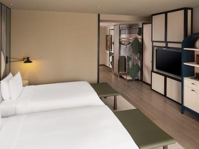 Moderner Hotelraum mit zwei großen Betten, hellem Holz und minimalistischem Design.