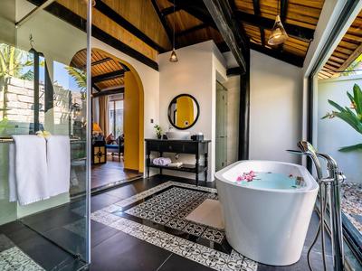 Moderne ligbad in een open badkamer met glazen wanden en tuinzicht.