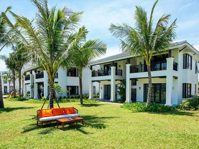 Moderne weiße Ferienwohnungen mit Balkonen, umgeben von grüner Wiese und Palmen.