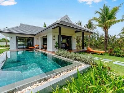 Modern huis met zwembad en palmbomen in de tuin onder een blauwe lucht.