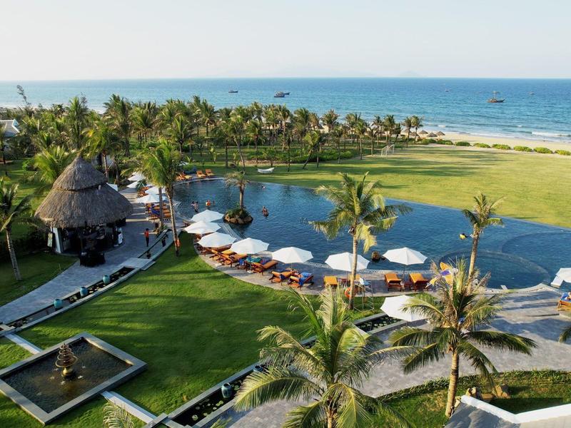 Luxe resort met zwembad, palmbomen en uitzicht op de oceaan bij heldere lucht.