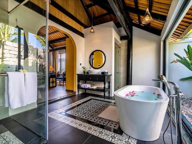 Moderne ligbad in een open badkamer met glazen wanden en tuinzicht.