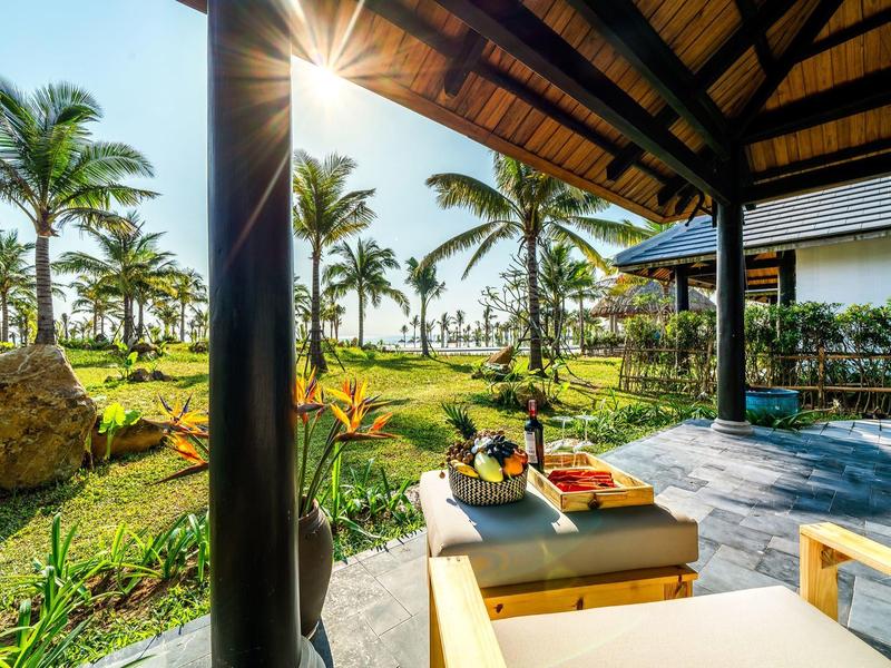 Terras in zonlicht met wijn en snacks, uitzicht op tropische palmbomen en tuin.