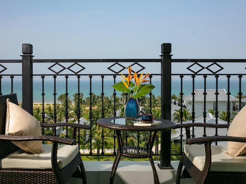 Balkon met stoelen, tafel, planten en uitzicht op zee bij heldere hemel.