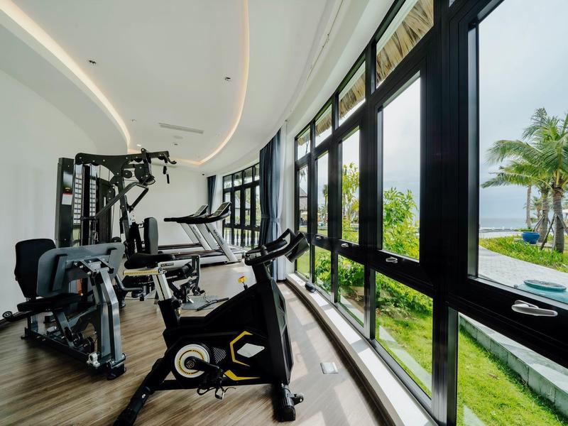 Fitnessruimte met moderne apparatuur en grote ramen met uitzicht op palmbomen en zee.