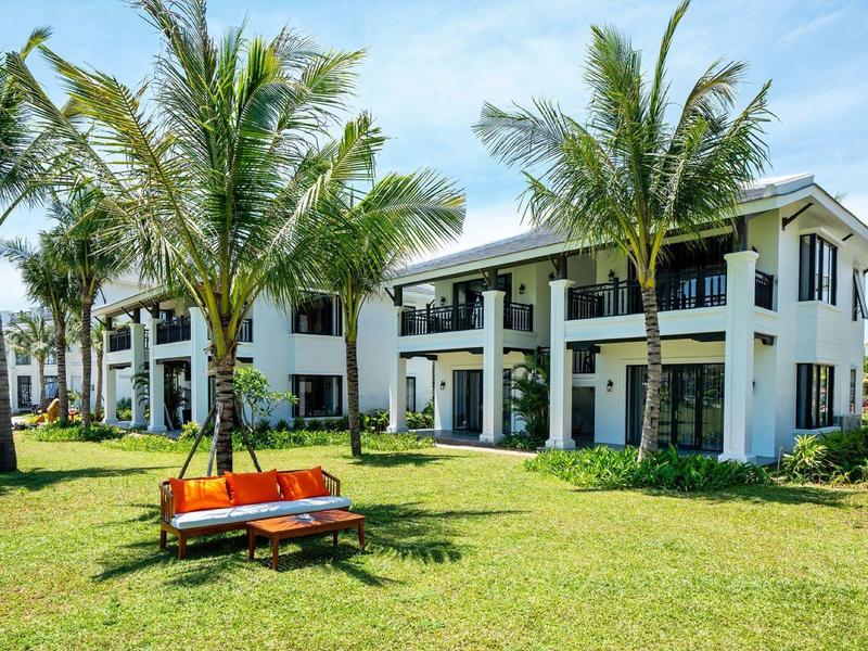 Modern tweeverdiepingen hotelcomplex met palmbomen en oranje banken op groen gras.