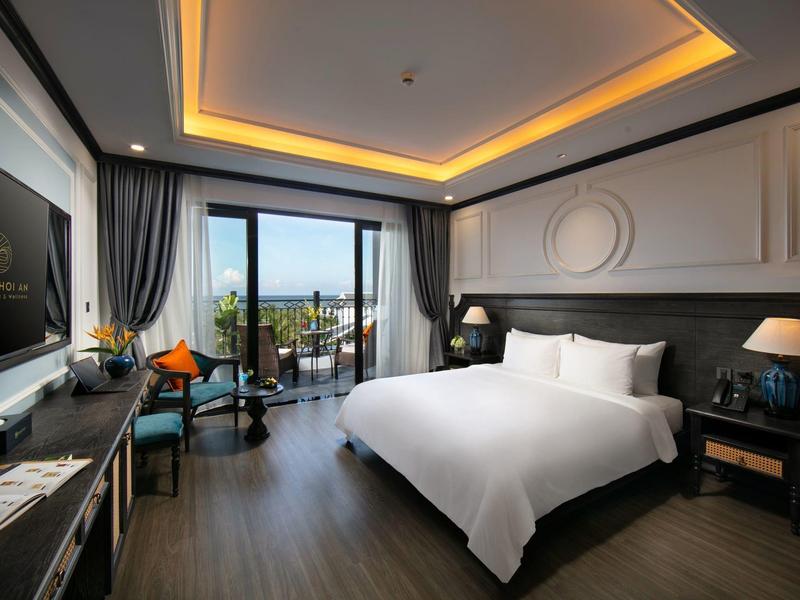 Modern hotelkamer met groot bed, bureau en balkon met uitzicht op groen.