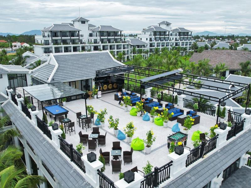 Dakterras van een hotel met zitgedeeltes, planten en uitzicht op andere hotelgebouwen.