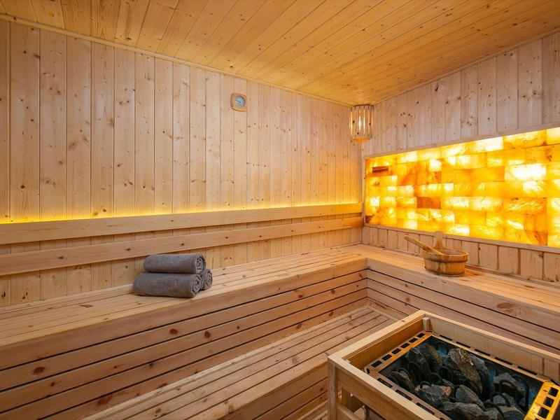 Lichte houten sauna met zoutstenen wand, stoomkachel en opgevouwen handdoeken.