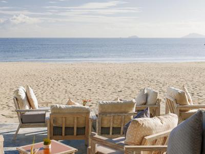 Strandterras met comfortabele zitplaatsen en uitzicht op zee onder bewolkte lucht.