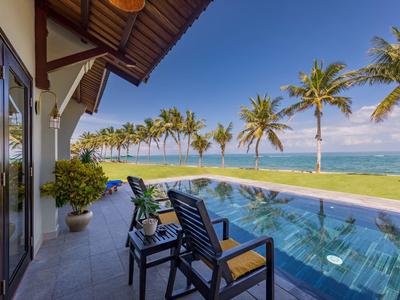 Terrasse mit Stühlen, Pool und Blick auf Palmen und Meer an einem sonnigen Tag.