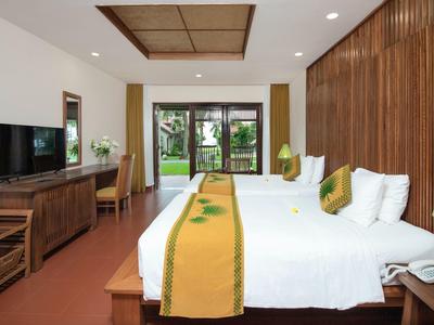 Lichte hotelkamer met twee bedden, houten meubels en uitzicht op de tuin.