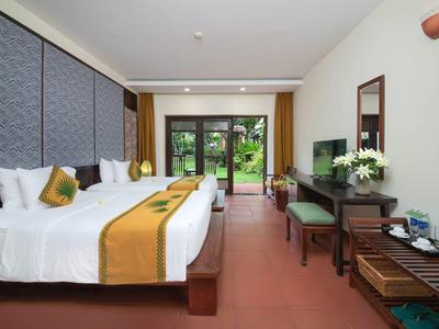 Hotelkamer met twee bedden, tv, bureau en uitzicht op een tuin.