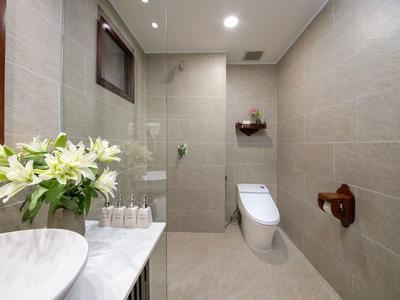 Moderne badkamer met beige betegelde muren, toilet, glazen douche en bloemen op het marmeren aanrecht.