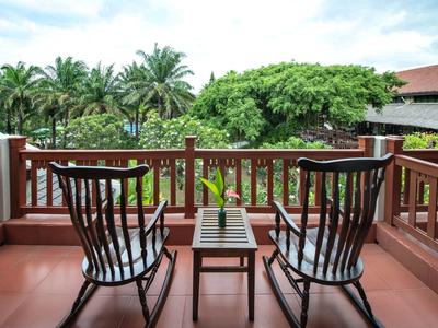Twee schommelstoelen en een kleine tafel op een balkon met uitzicht op tropische planten.