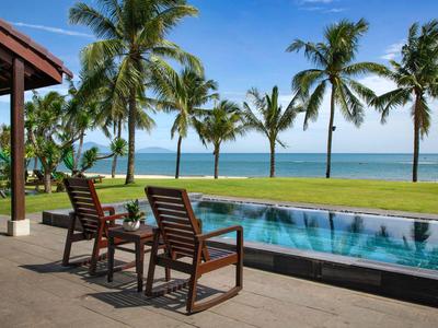 Zwei Holzstühle neben einem Pool mit Blick auf Palmen und das Meer.