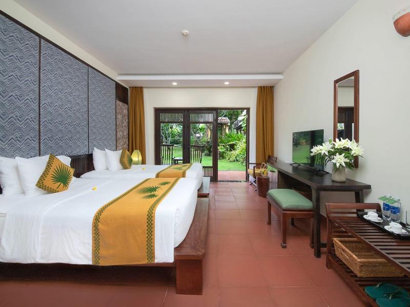 Hotelkamer met twee bedden, tv, bureau en uitzicht op een tuin.