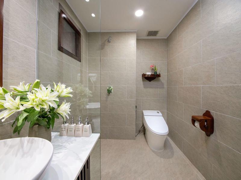 Moderne badkamer met beige betegelde muren, toilet, glazen douche en bloemen op het marmeren aanrecht.