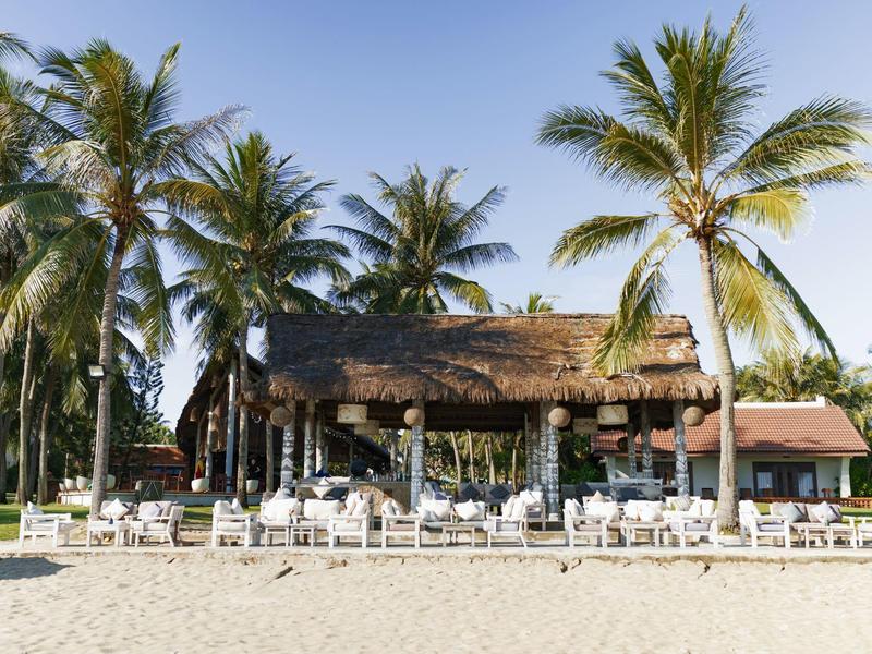 Overdekte zitgedeeltes met houten meubels met uitzicht op een zandstrand en de zee.