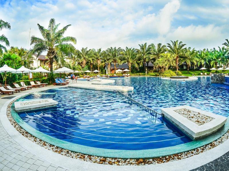 Groot hotelzwembad met palmbomen en ligstoelen onder een blauwe hemel.