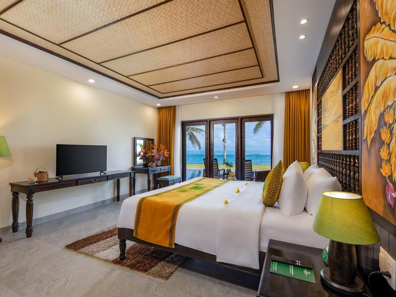 Modern ingerichte hotelkamer met tweepersoonsbed, tv en zeezicht door grote ramen.