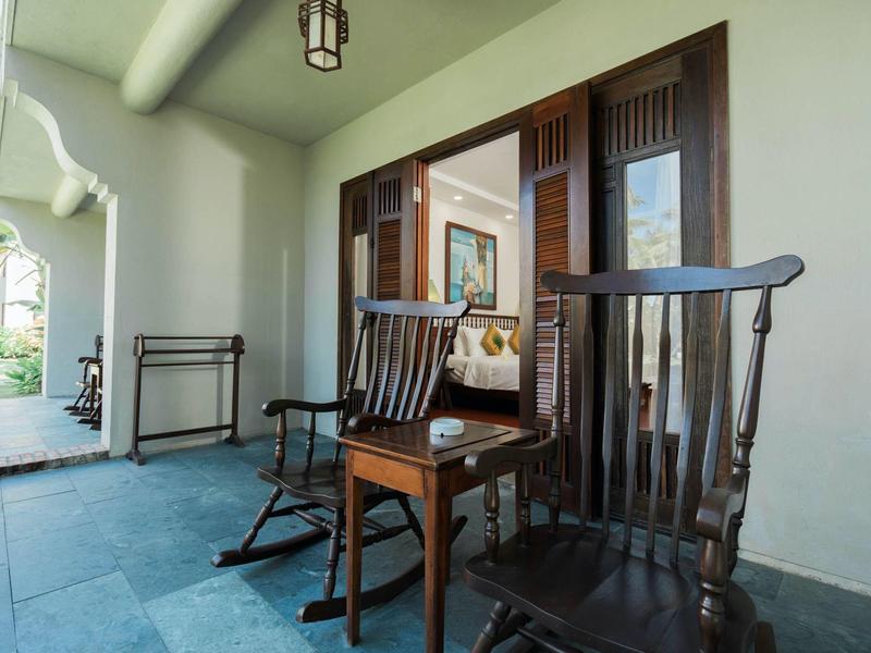 Twee zwarte houten schommelstoelen met een klein houten tafeltje op een veranda naast een schuifdeur