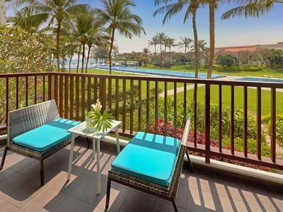 Balkon mit Stühlen und Tisch mit Pool und Palmen im Hintergrund.