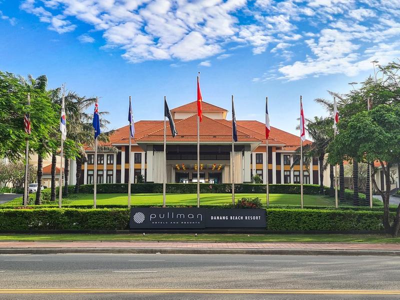 Edificio con tetti rossi circondato da alberi e bandiere sotto un cielo sereno