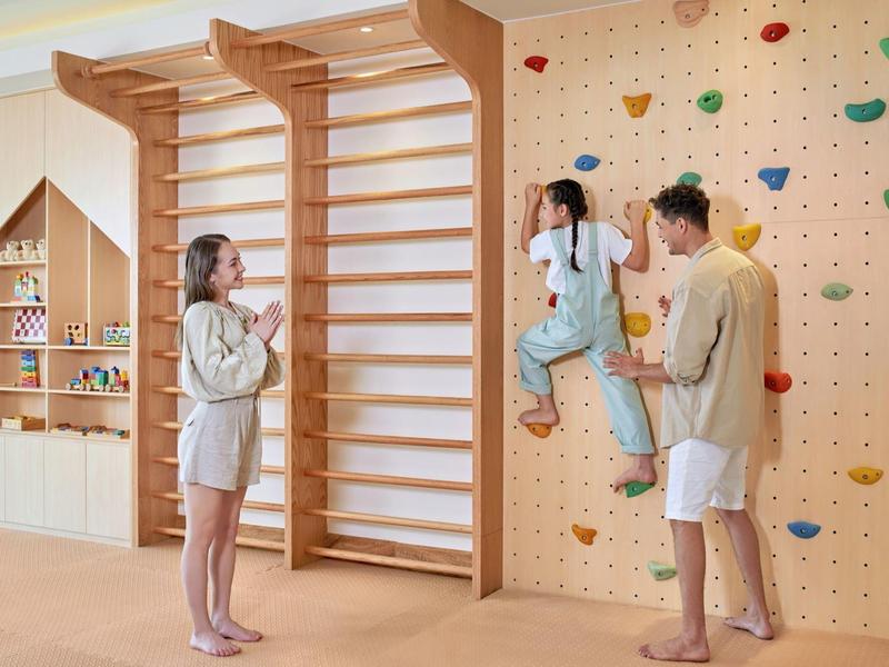 Genitori osservano i bambini arrampicarsi su una parete da arrampicata in una stanza giochi luminosa.