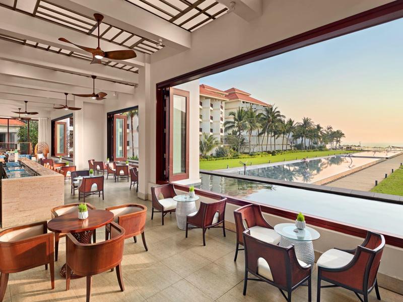 Sala da pranzo aperta con vista su piscina, palme e edificio dell'hotel al tramonto.