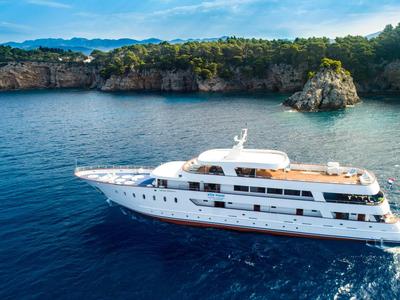 Luxury white yacht sailing in clear blue water near rocky coast with green vegetation.