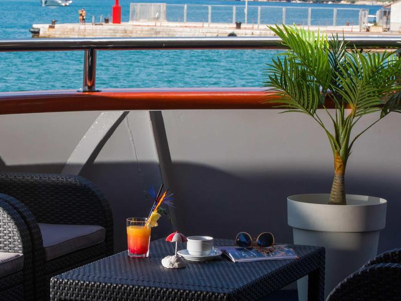 Seating area on a terrace with drinks overlooking harbor and mountains.