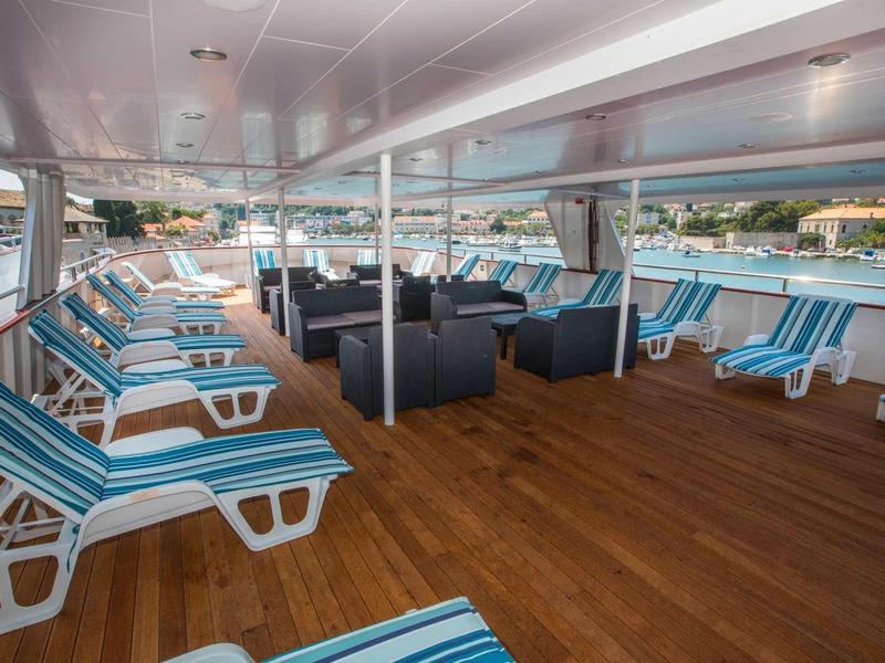 Covered outdoor area on a ship with blue lounge chairs and seating groups.