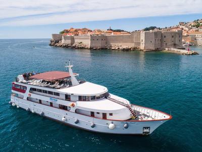 Weißes Passagierschiff fährt auf blauem Meer vor einer befestigten historischen Küstenstadt.