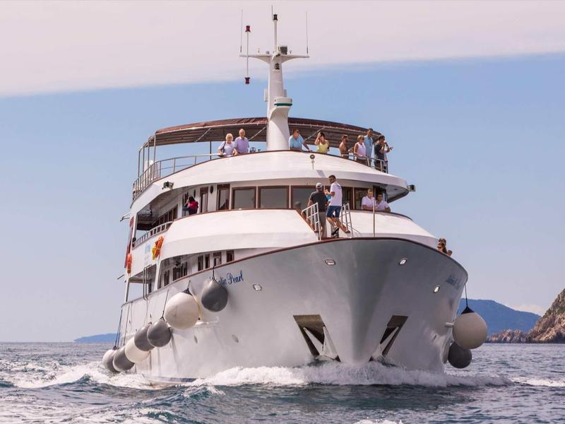 Große weiße Yacht fährt auf ruhigem Meer nahe felsiger Küste unter klarem Himmel.