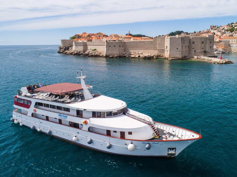 Weißes Passagierschiff fährt auf blauem Meer vor einer befestigten historischen Küstenstadt.