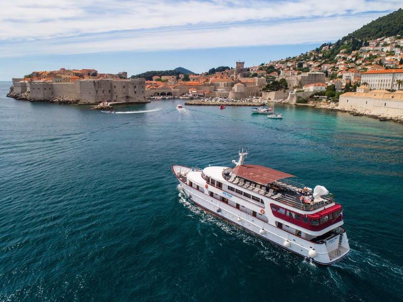 Großes weißes Kreuzfahrtschiff fährt auf blauem Wasser vor einer Küstenstadt mit historischer Altstadt.