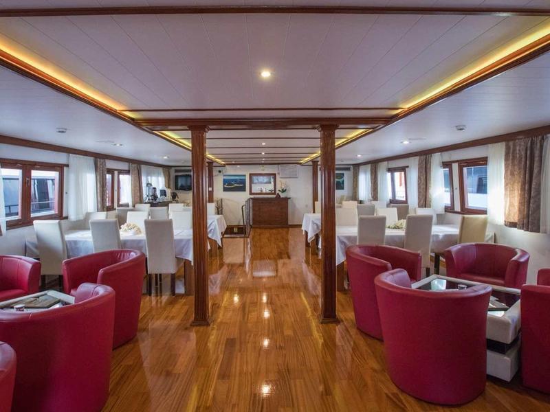 Luxuriöser Salon mit roten Sesseln, Holzfußboden und großen Fenstern an Bord eines Schiffes.