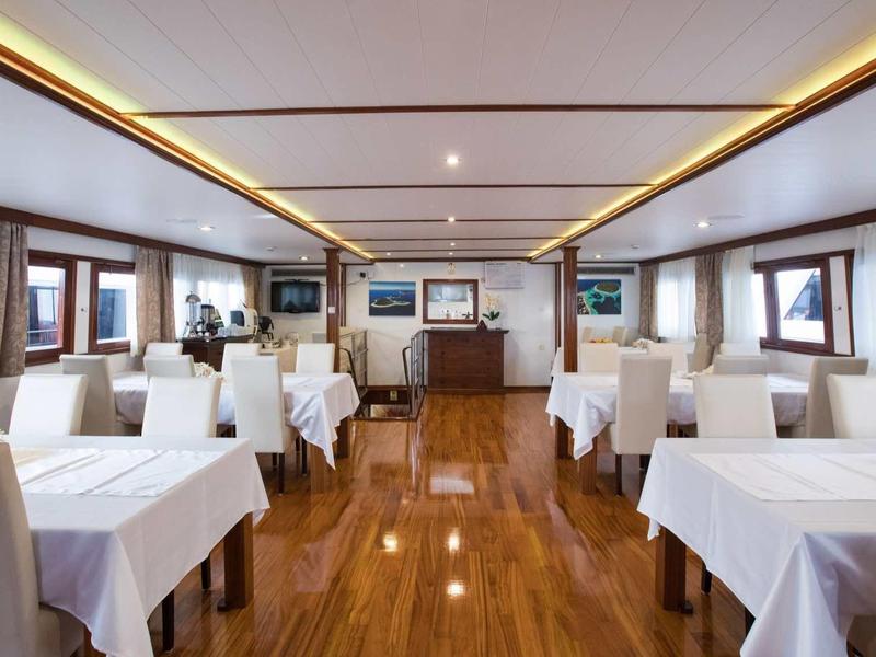 Gemütlicher Speiseraum mit weißen Tischdecken, Holzboden und warmem Deckenlicht.