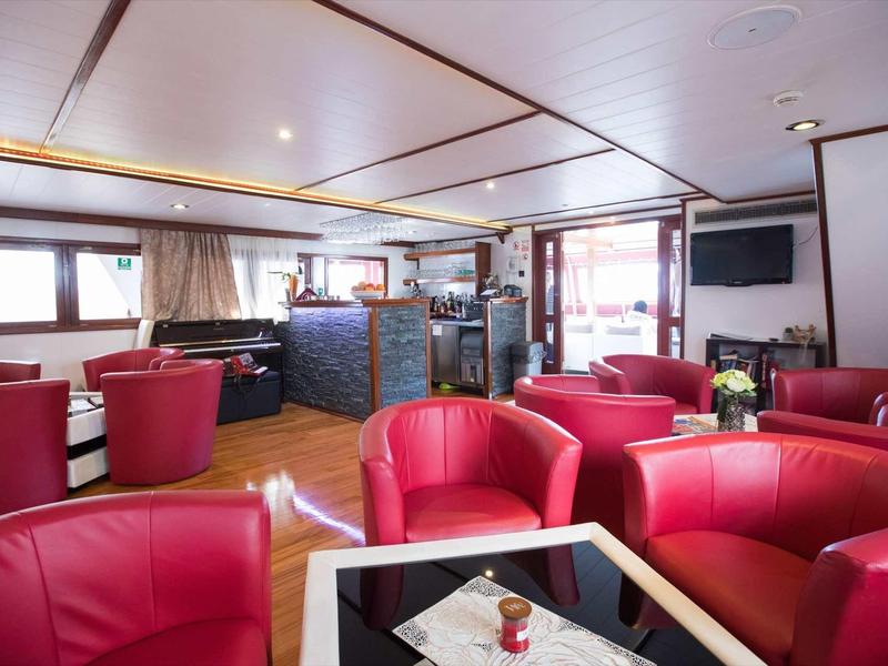 Gemütlicher Salon mit roten Lederstühlen, Tischdecken, großen Fenstern und hellem Holzdekor.