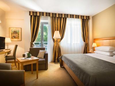 Cozy hotel room with large bed, seating area, desk, and curtains on windows.