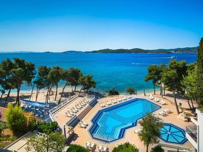 Blick auf einen Hotelpool mit Sonnenschirmen und Blick auf das blaue Meer und den Himmel.