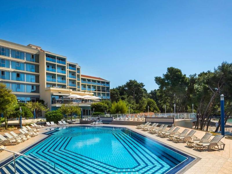 Modern hotel pool area with sun loungers beside a sea view under clear sky.