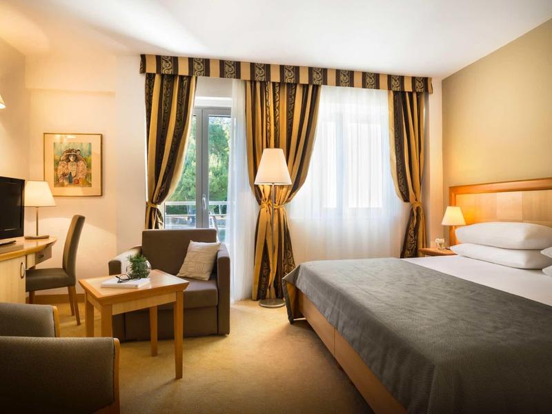 Cozy hotel room with large bed, seating area, desk, and curtains on windows.