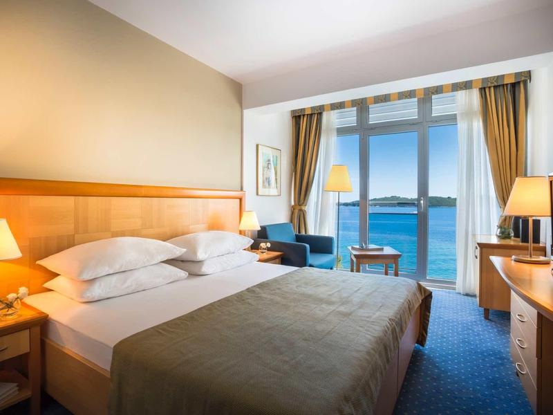 Bright hotel room with large bed, sea view, and modern furnishings.