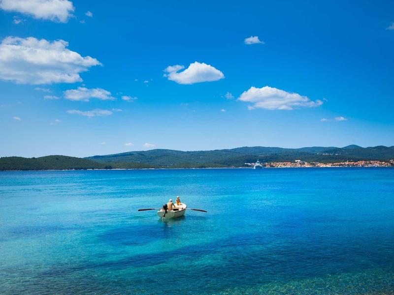 Clear blue sea with a boat and two people under a sunny sky.