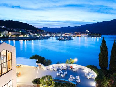 Widok na oświetlony teren hotelowy nad wodą z górami w tle o zmierzchu.