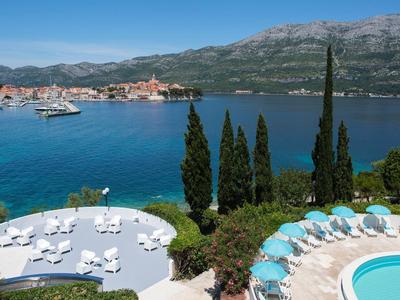 Widok na teren basenu z leżakami i morzem w tle pod czystym niebem.