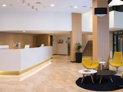 Moderne Hotellobby mit Empfangstresen, Stühlen und Tisch, helle Beleuchtung und Holzverkleidung.