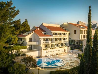 Hotelgebäude mit Terrassen und rundem Pool, umgeben von grünen Bäumen bei Sonnenuntergang.
